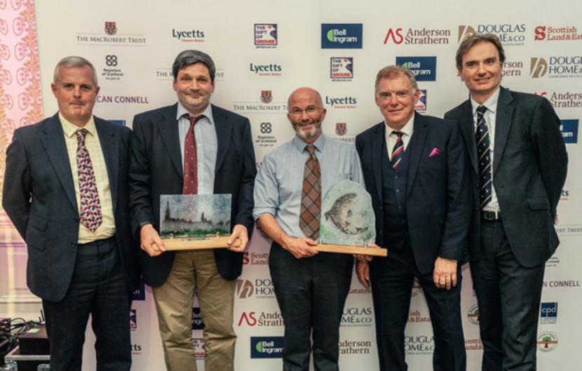 5 men in suits, standing and holding 2 awards.