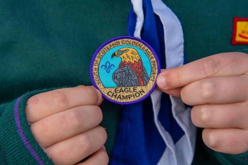 Child in a Scouts uniform holding a 'golden eagle champion' badge.
