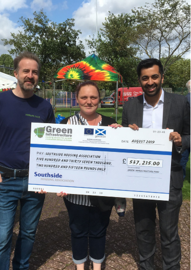 three people outdoors holding a cheque