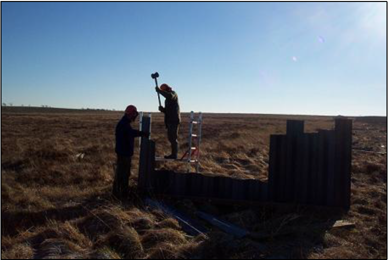 two people hammering piles starting from centre of ditch