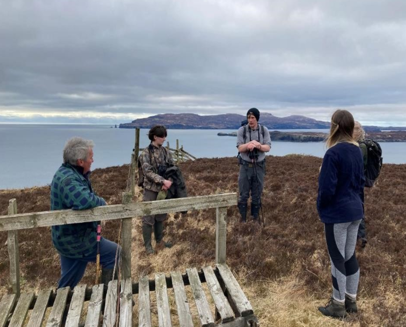 staff standing meeting in a field, with sea in the background.