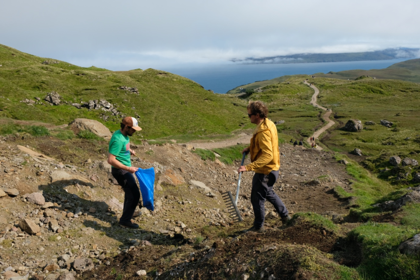 2 workers carrying out repair work on footpath with the sea in the distance.