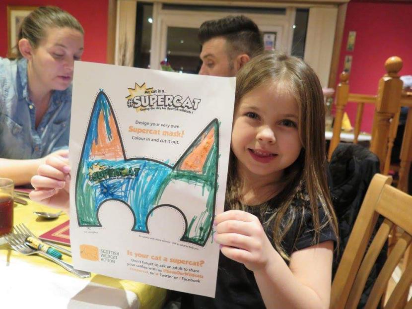 A young girl shows a #supercat mask she has coloured-in.