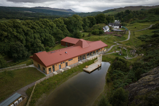 Wood clad building with a jetty in front, surrounded by woodland.