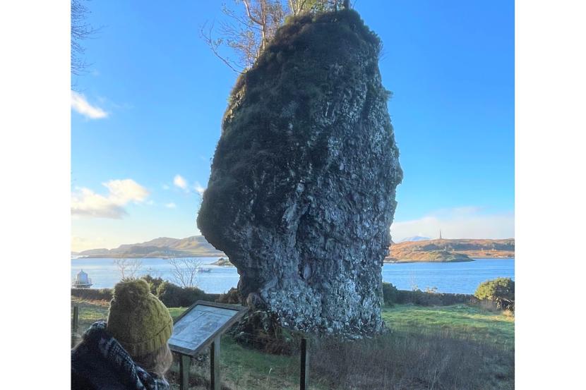 A person looking at a standing stone with river in the mid ground and hills in the background.