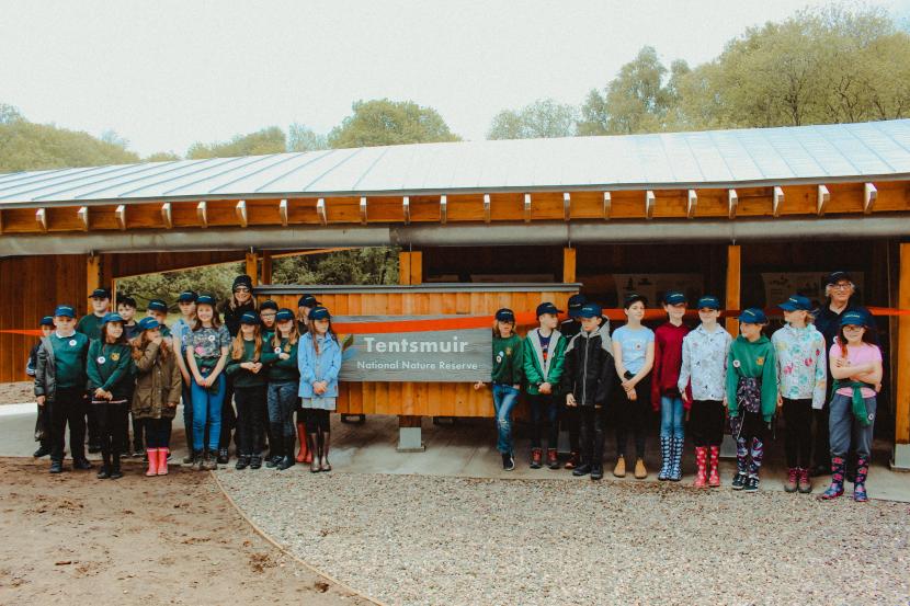 A group of school children, with NatureScot Staff standing outside new pavillion.