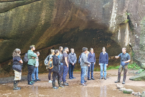 NNR Staff talking to a group of students, in the reserve - with high rocks on one side.