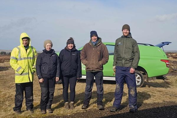A group of people in outdoor gear standing beside a car.