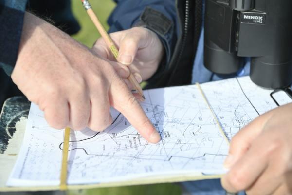 A paper map with hands holding it, and another hand pointing to a spot on the map