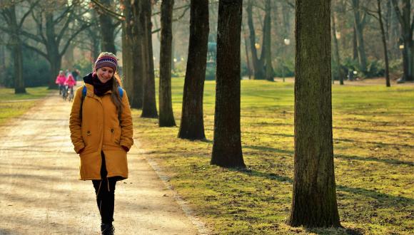 Female walking in park in warm jacket, with kids on bike in background
