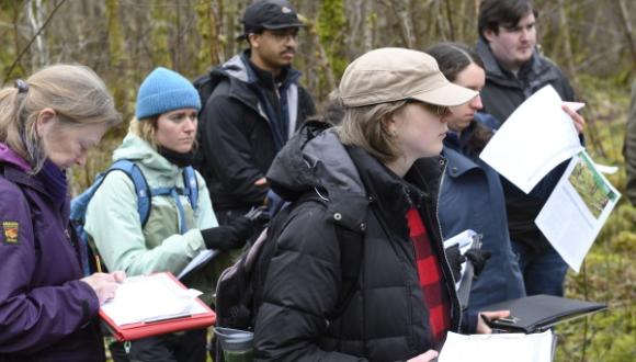 A group of young people standing in a woodland, in outdoor clothing.